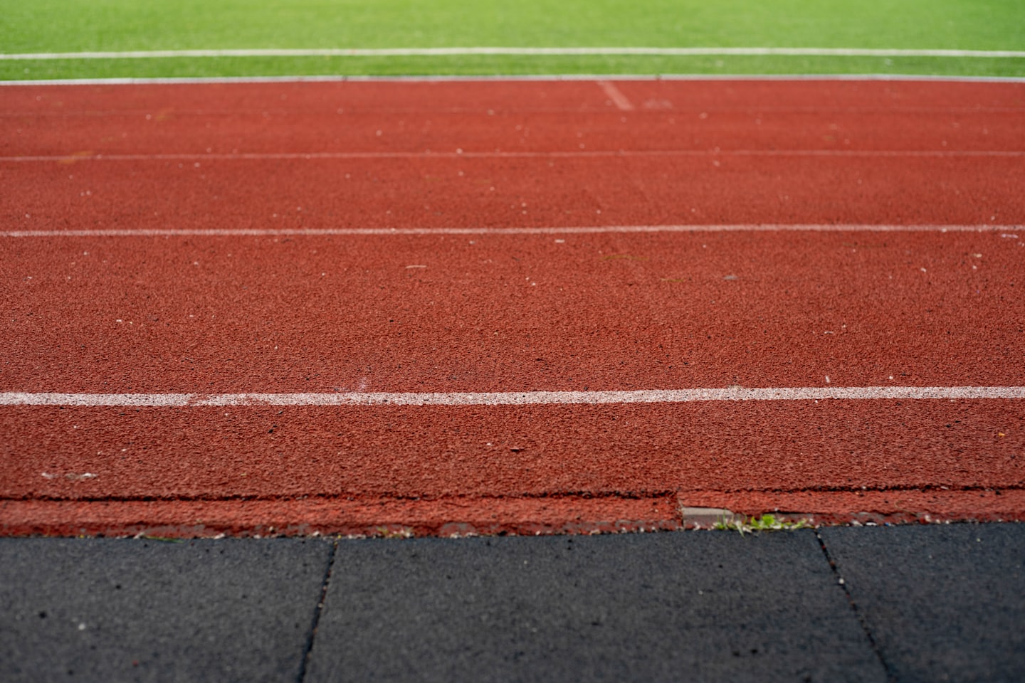 Segnaletica orizzontale bianca divide una pista di atletica rossa.