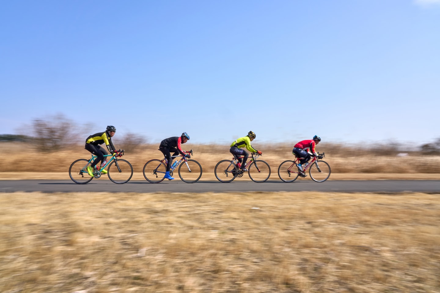 Quattro ciclisti in fila indiana su una strada asfaltata.